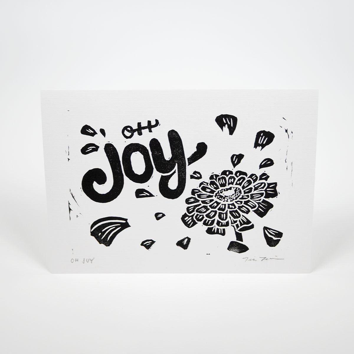 White paper with "Oh Joy" hand lettering with an illustration of a zinnia with petals floating around the text.