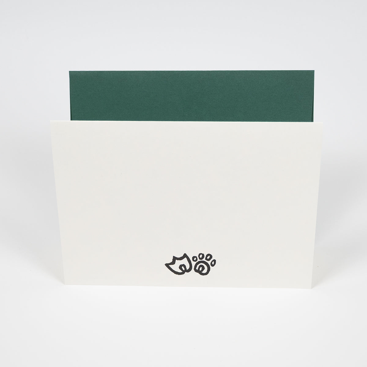 White greeting card with duck paw and cat paw illustrations in front of a dark green envelope.