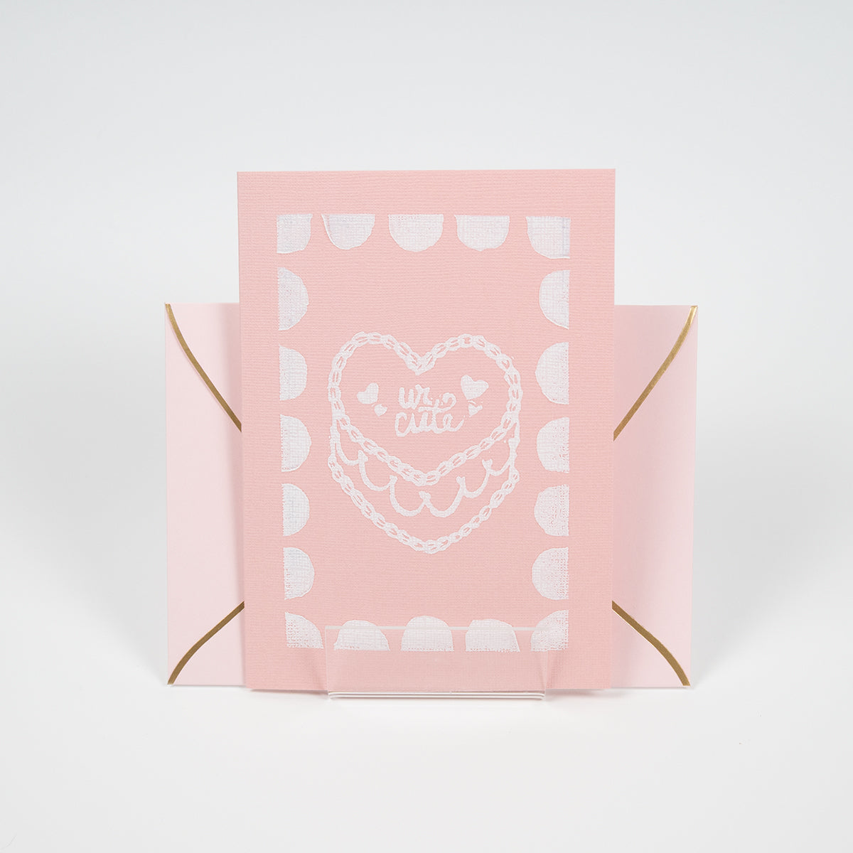 Light coral greeting card with a"ur cute" cake illustration in front of a light pink envelope.