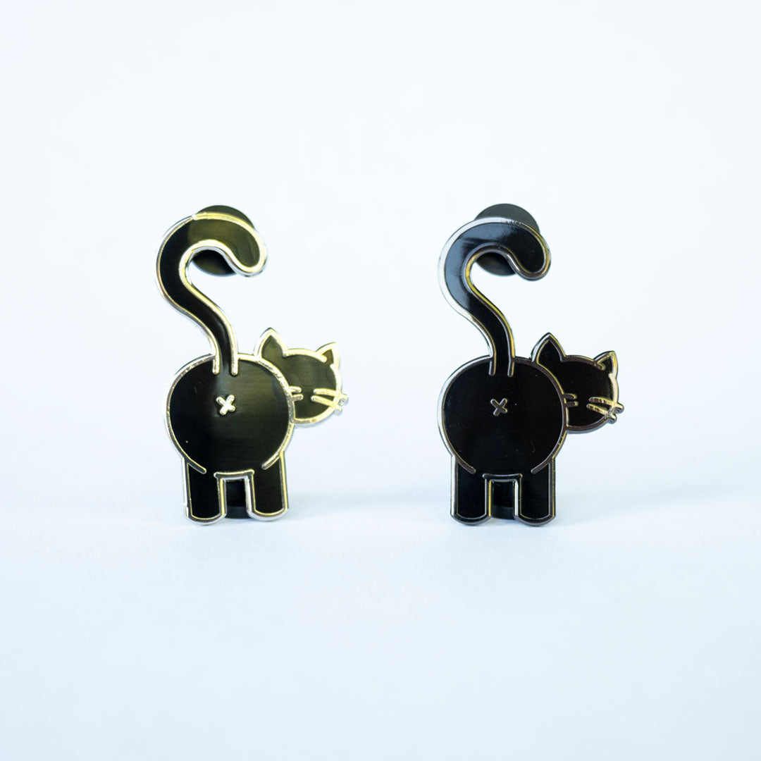Black cat butt pin with silver metal on left and a black cat butt pin with black nickel metal on right on white background.