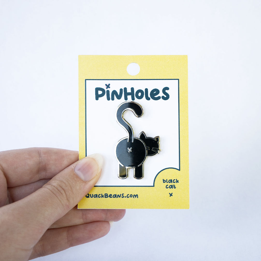 Hand holding black cat butt pin on yellow Pinholes hang tag card.