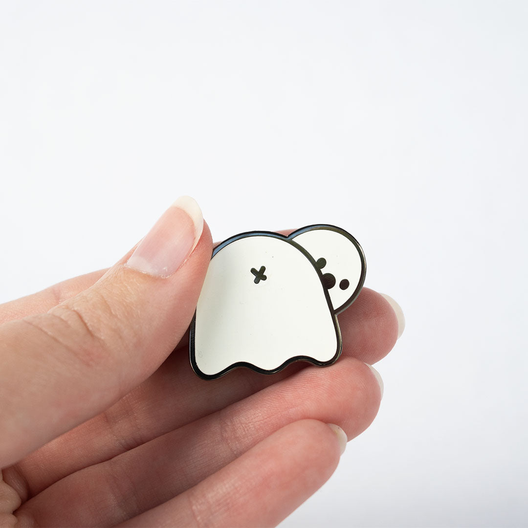 Hand holding white, glow in the dark ghost butt pin