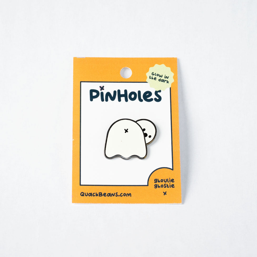 Glow in the dark ghost butt pin on a orange backing card with the word "Pinholes"