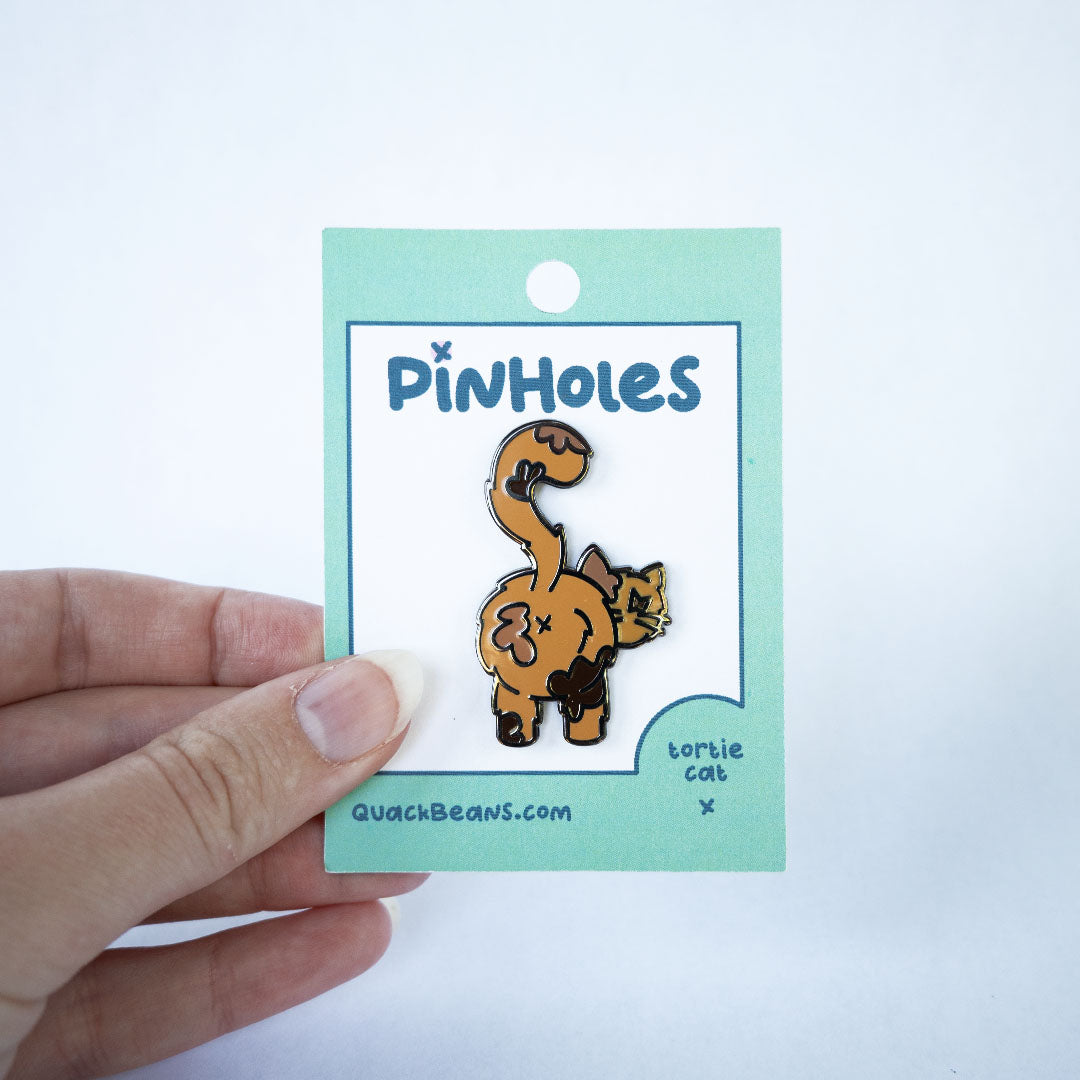 Hand holding tortoiseshell cat butt pin on green Pinholes hang tag card.