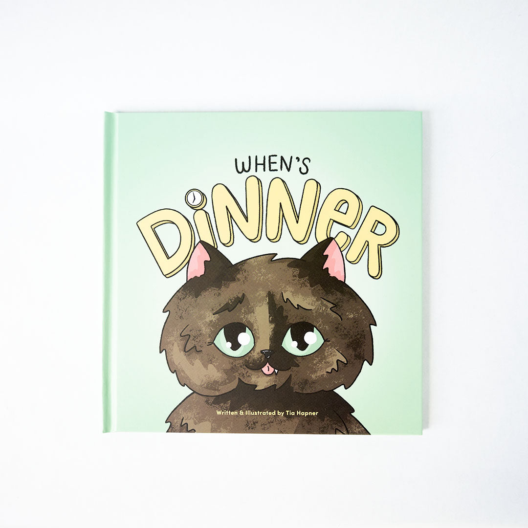 When's Dinner book front cover with a smiling tortoiseshell kitty with the handlettered text, "When's Dinner"