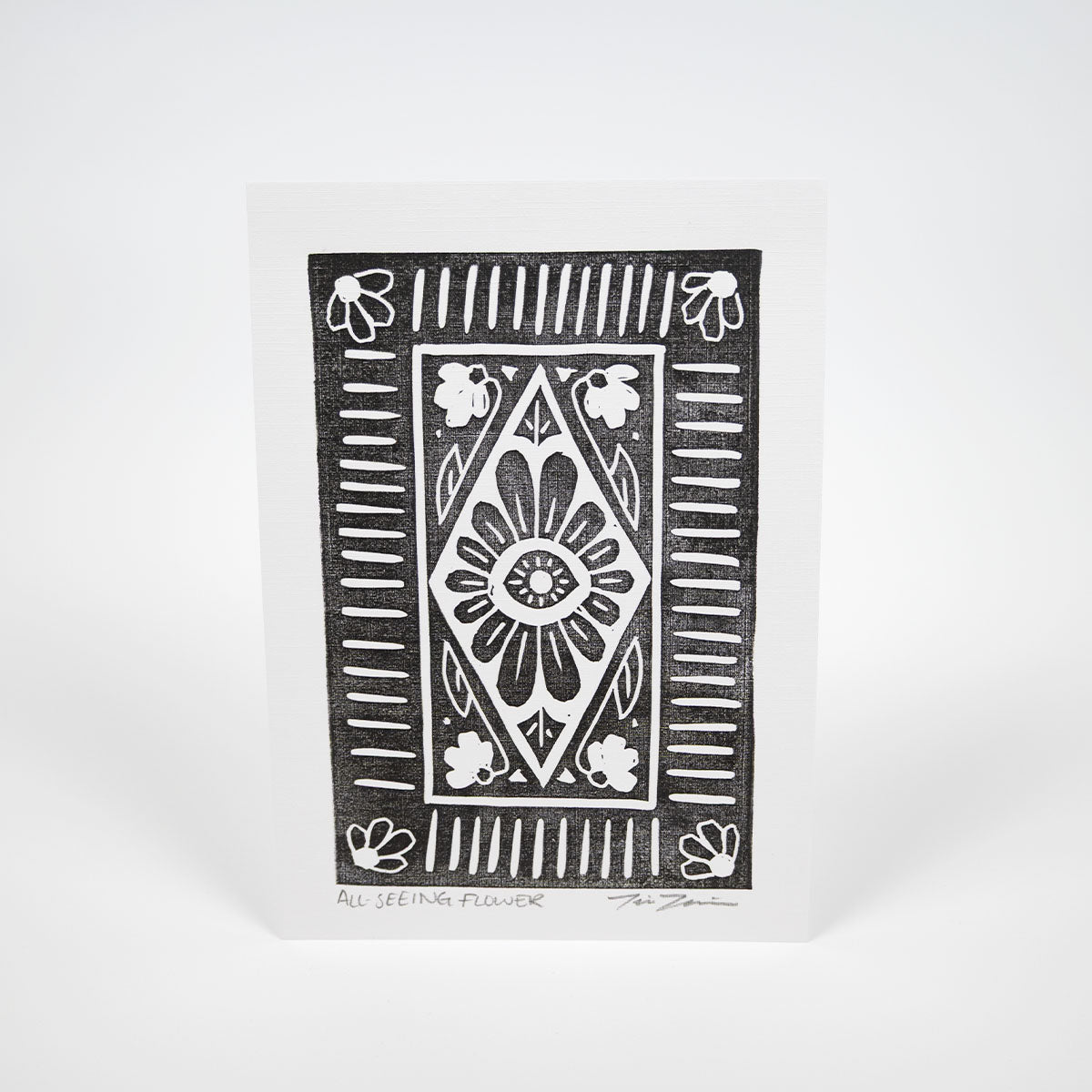 A black stylized illustration of a flower with an eye in the center surrounded by various lines and flowers on white paper. 