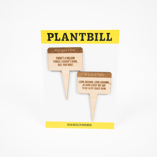 White and yellow card with "Plantbill" across the top and "Hamilthorn" across the bottom. In the middle are two wooden plant/garden stakes with "There's a million things I haven't done. Just you wait.," and "Look around, look around, at how lucky we are to be alive right now" engraved on them.