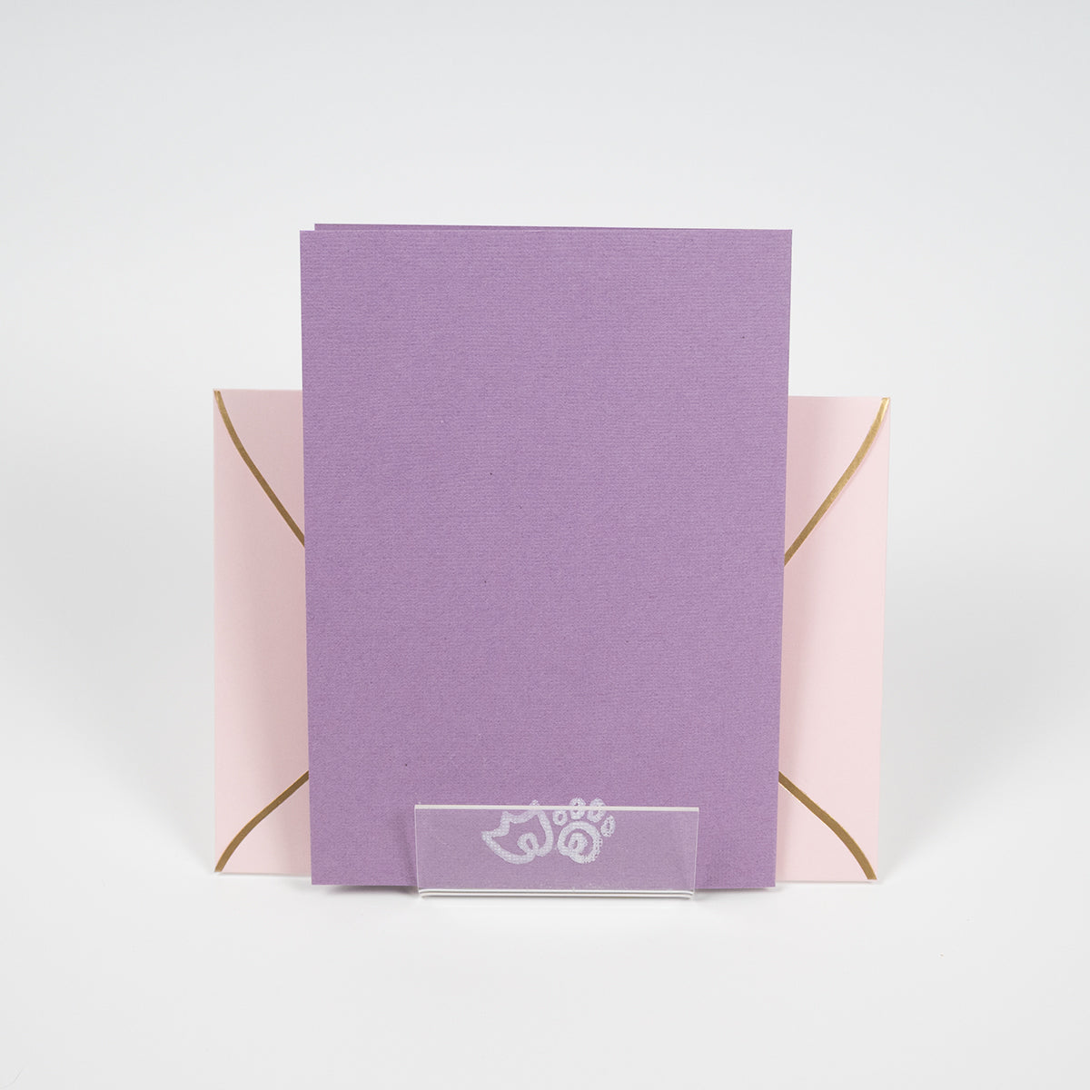 Purple greeting card with a duck paw and cat paw illustration in front of a light pink envelope. 