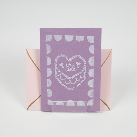 Purple greeting card with a"ur cute" cake illustration in front of a light pink envelope. 